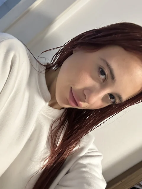 Natalye with red hair taking a selfie in a cream sweater